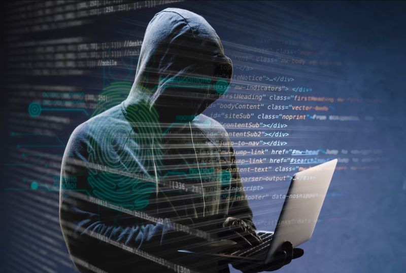 Hacker in hoody looking at a laptop